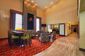 Un hall d’hôtel doté d’un tapis rouge à motifs, d’un plancher en bois, d’un mur décoratif en pierre et d’un espace salon avec des fauteuils à motifs floraux et une table.