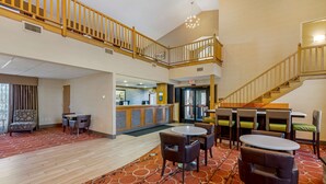 A spacious lobby with a high ceiling, a central seating area with tables and chairs, a reception desk, and a staircase leading to an upper level. - Best Western Falcon Plaza - Bowling Green (Bowling Green)