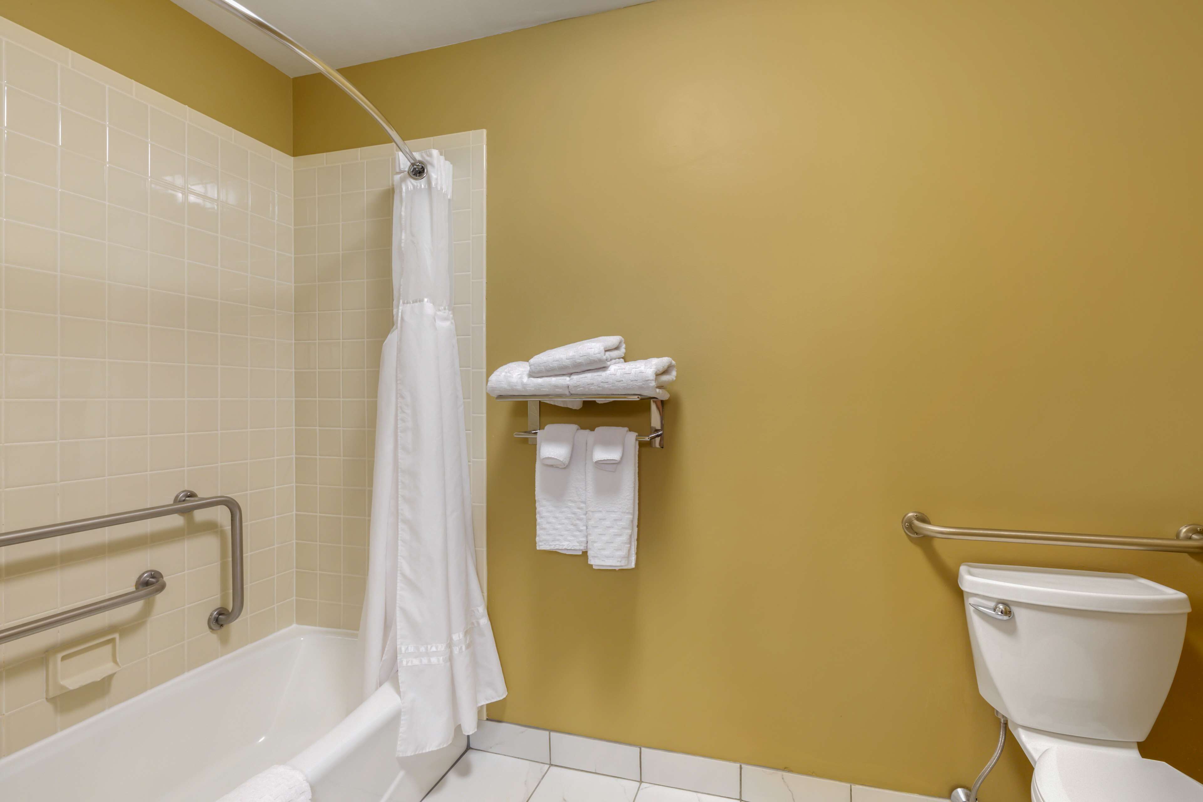 A bathroom with a bathtub, toilet, and shower curtain. There are white towels on a rack and a grab bar next to the bathtub.