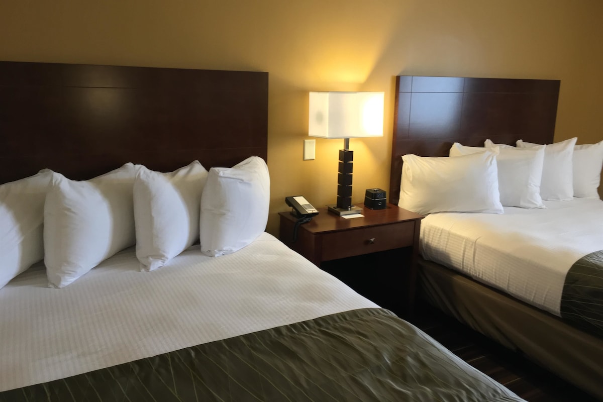 A hotel room with two beds, a nightstand with a lamp, and a telephone.