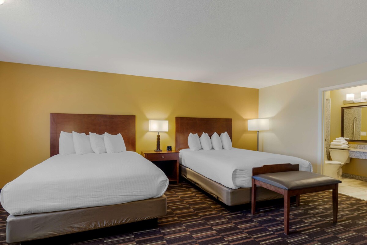 A hotel room with two beds, a small table, and a bathroom with a mirror and toilet.
