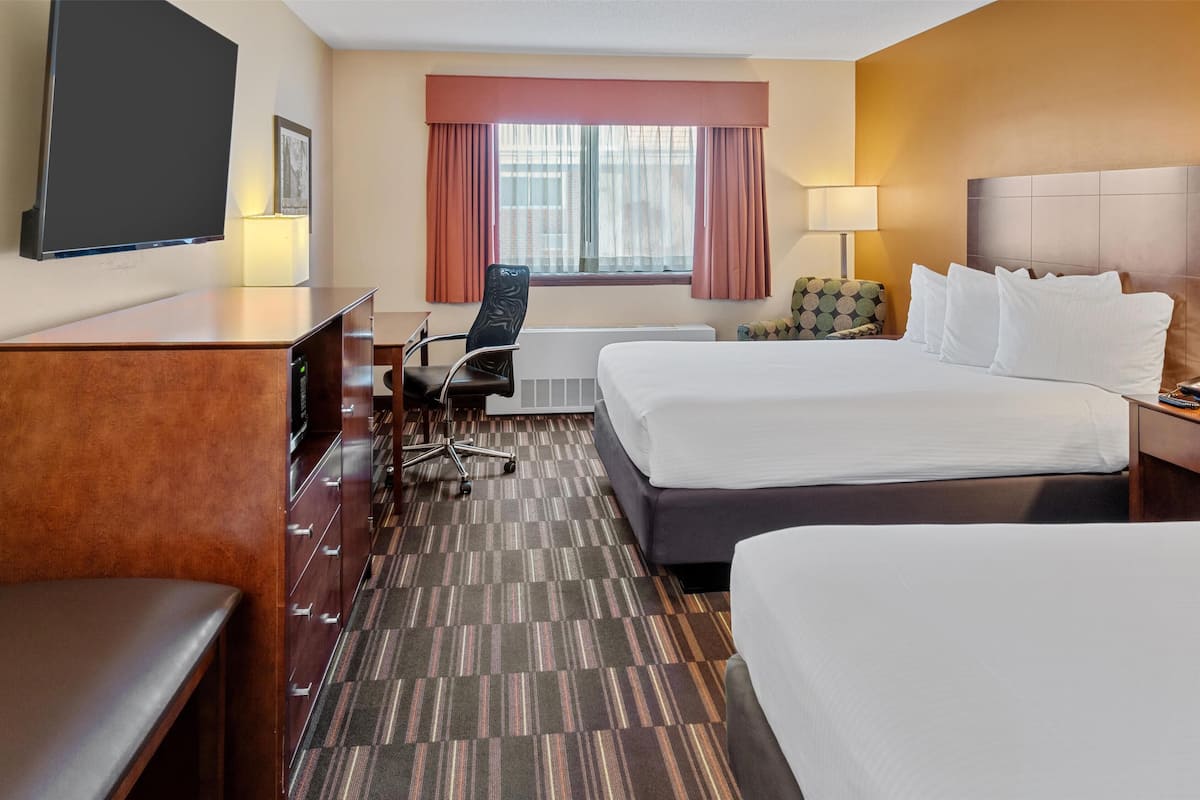 Une chambre d’hôtel avec deux lits, un bureau, une chaise, une télévision et une fenêtre avec des rideaux.