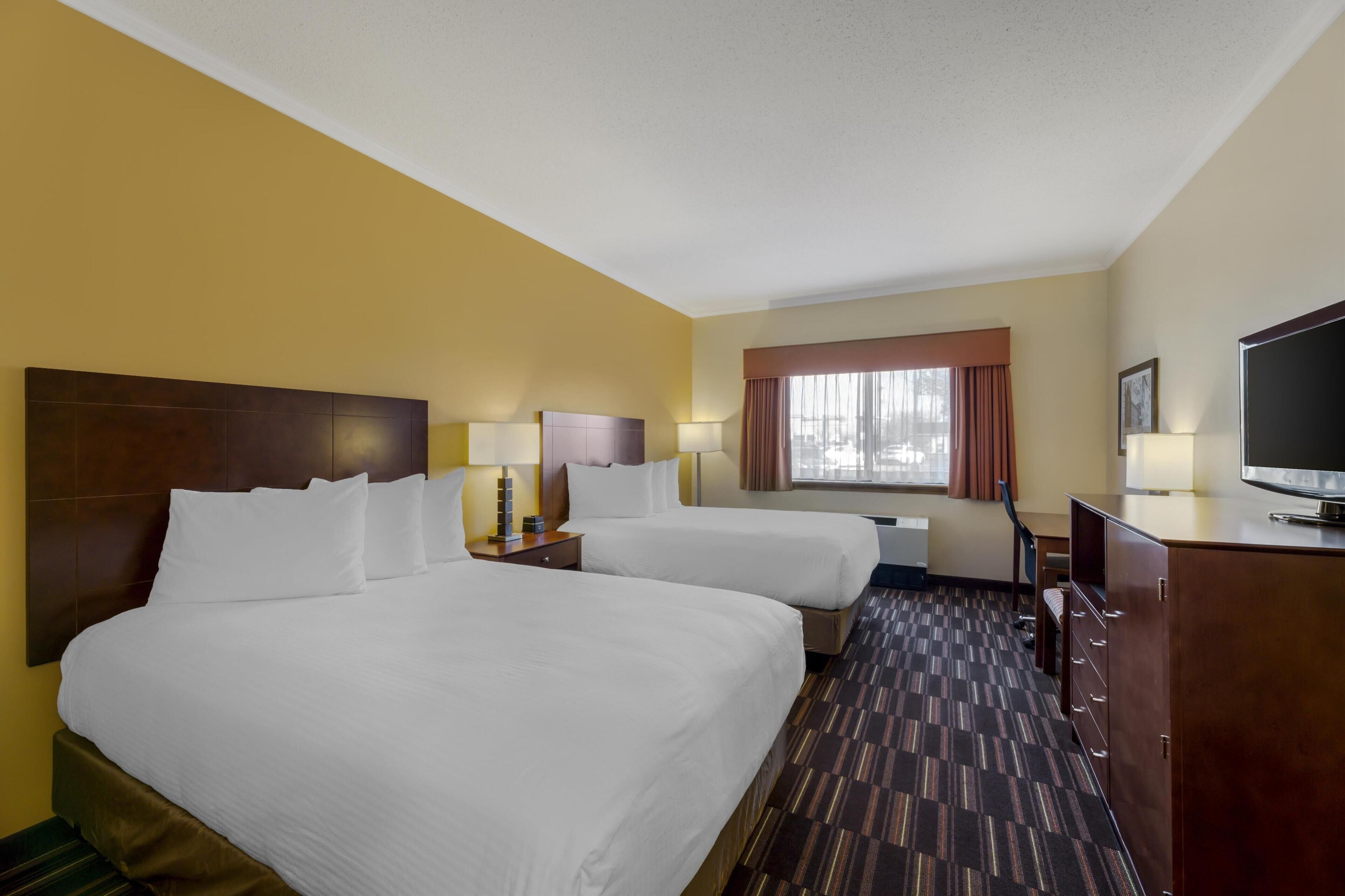 A hotel room with two beds, a television, a desk, and a window with curtains.