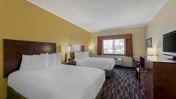 A hotel room with two beds, a television, a desk, and a window with curtains.