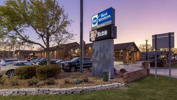 Une enseigne d’hôtel Best Western avec une horloge numérique indiquant 5 h 28, un parking avec plusieurs voitures et un bâtiment aux murs en briques et au toit plat.
