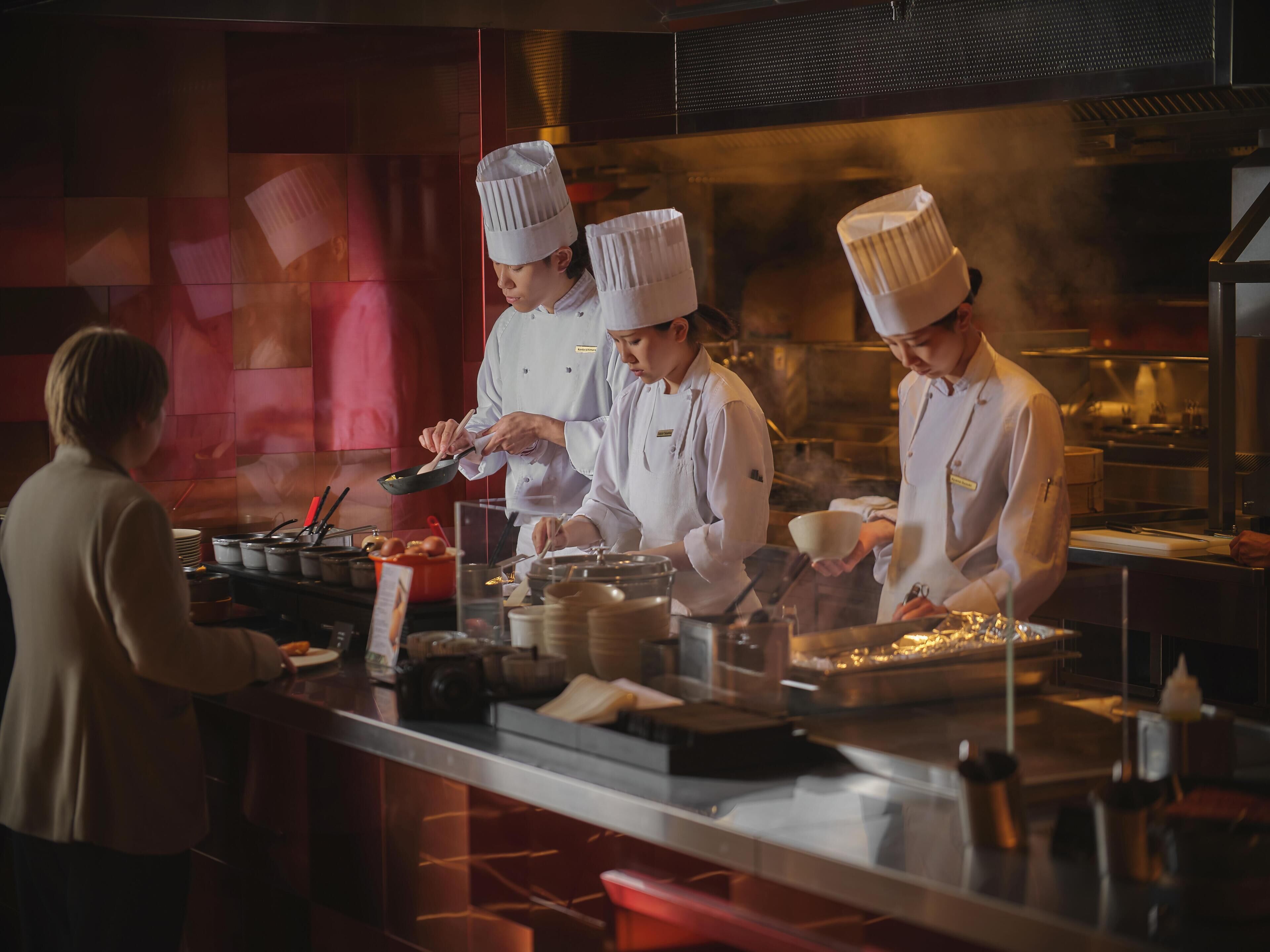 A professional kitchen with chefs preparing food, stainless steel counters, and cooking equipment.
