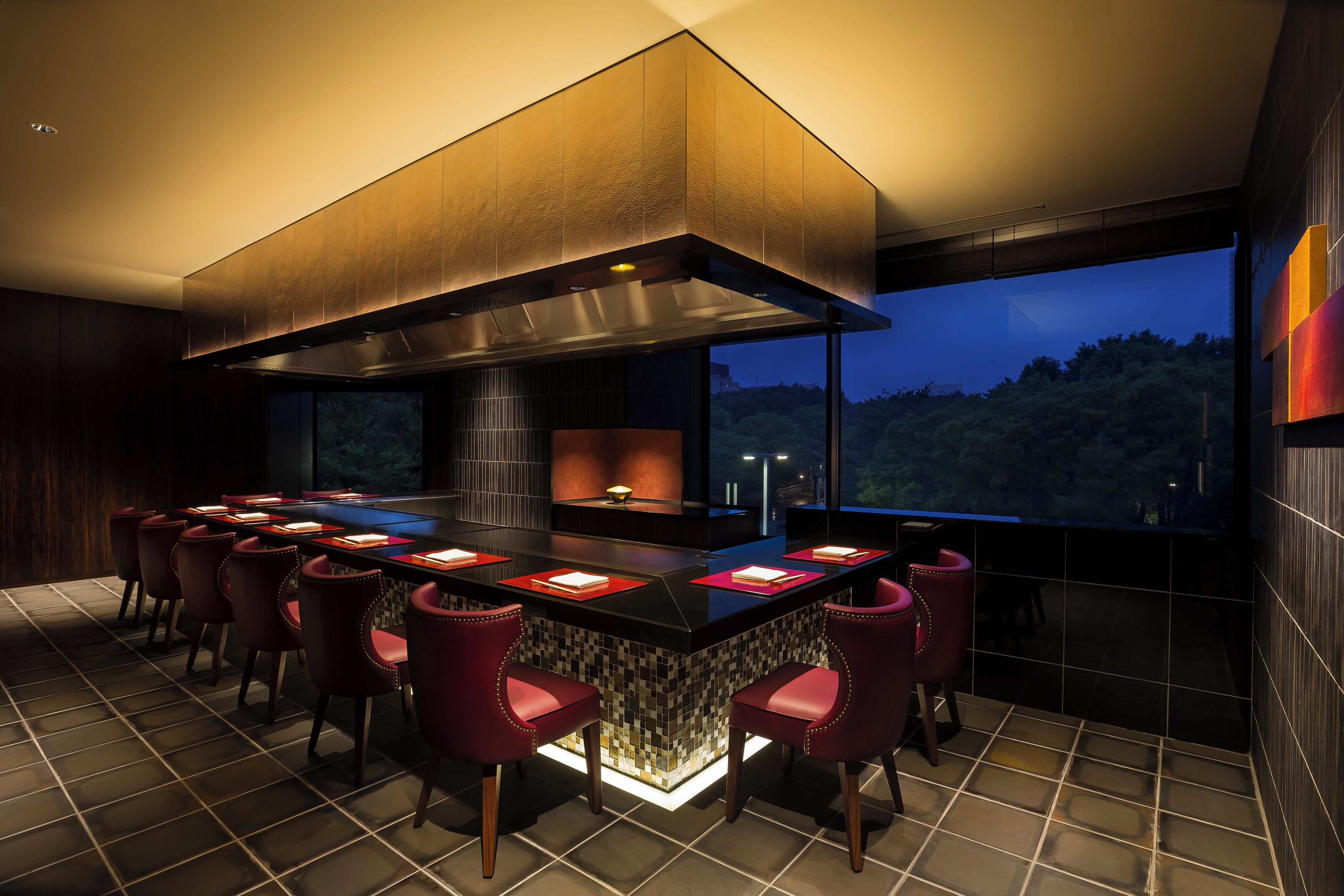 A modern kitchen with a central island, bar seating, and a large window overlooking a forested area.