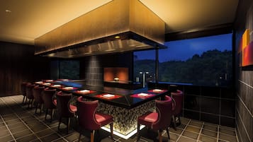 A modern kitchen with a central island, bar seating, and a large window overlooking a forested area.