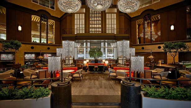 A spacious lobby with high ceilings, ornate chandeliers, and a central bar area.