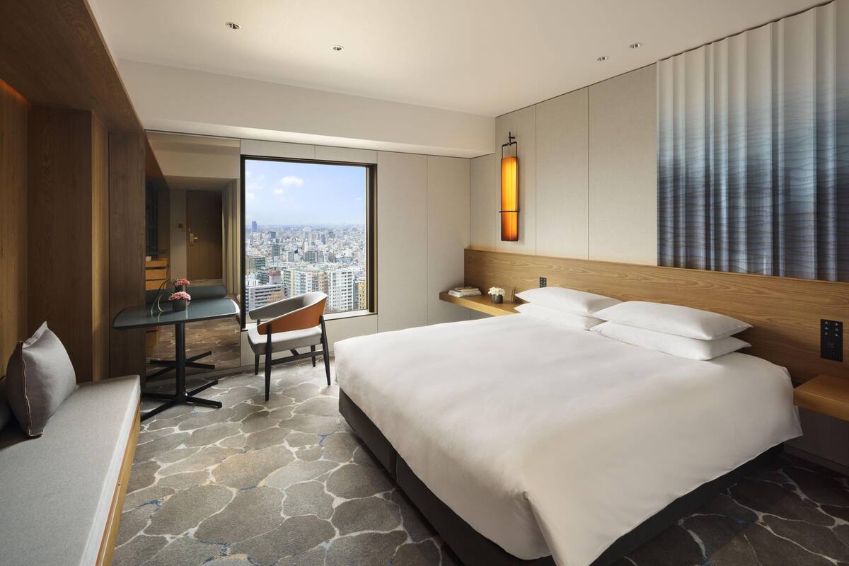 A hotel room with a large bed, a desk, a chair, a view of the city, and a modern design.