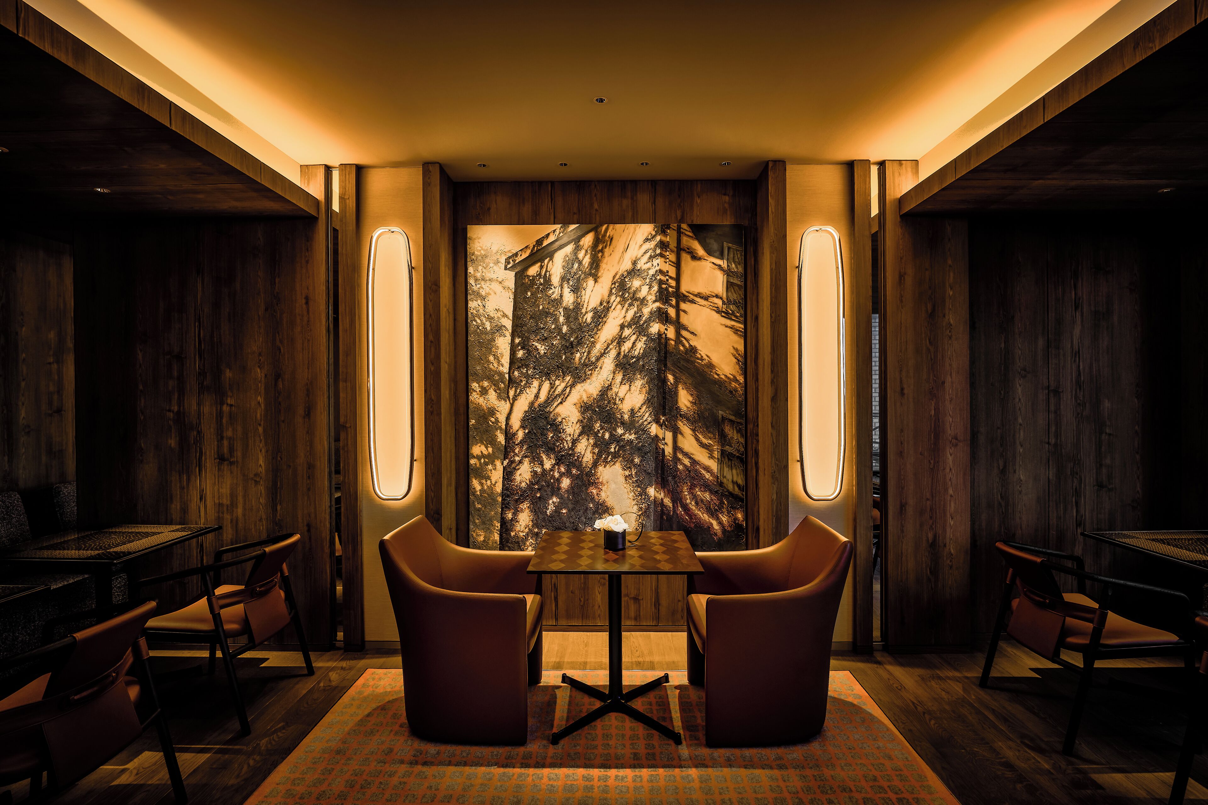 A cozy dining area with a table and chairs, a large illuminated artwork on the wall, and wooden paneling.