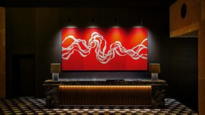 A reception area with a red abstract wall art, two wall-mounted lamps, a marble counter, and a patterned floor.