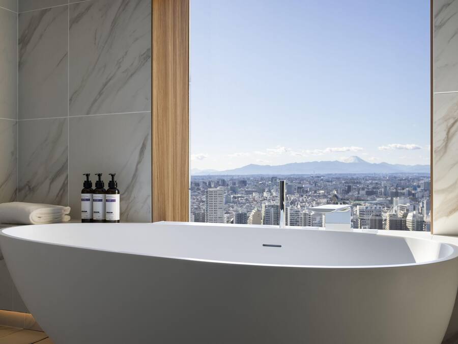 Une salle de bain moderne avec une baignoire sur pieds, des murs en marbre, une vue sur la ville et des articles de toilette à portée de main.