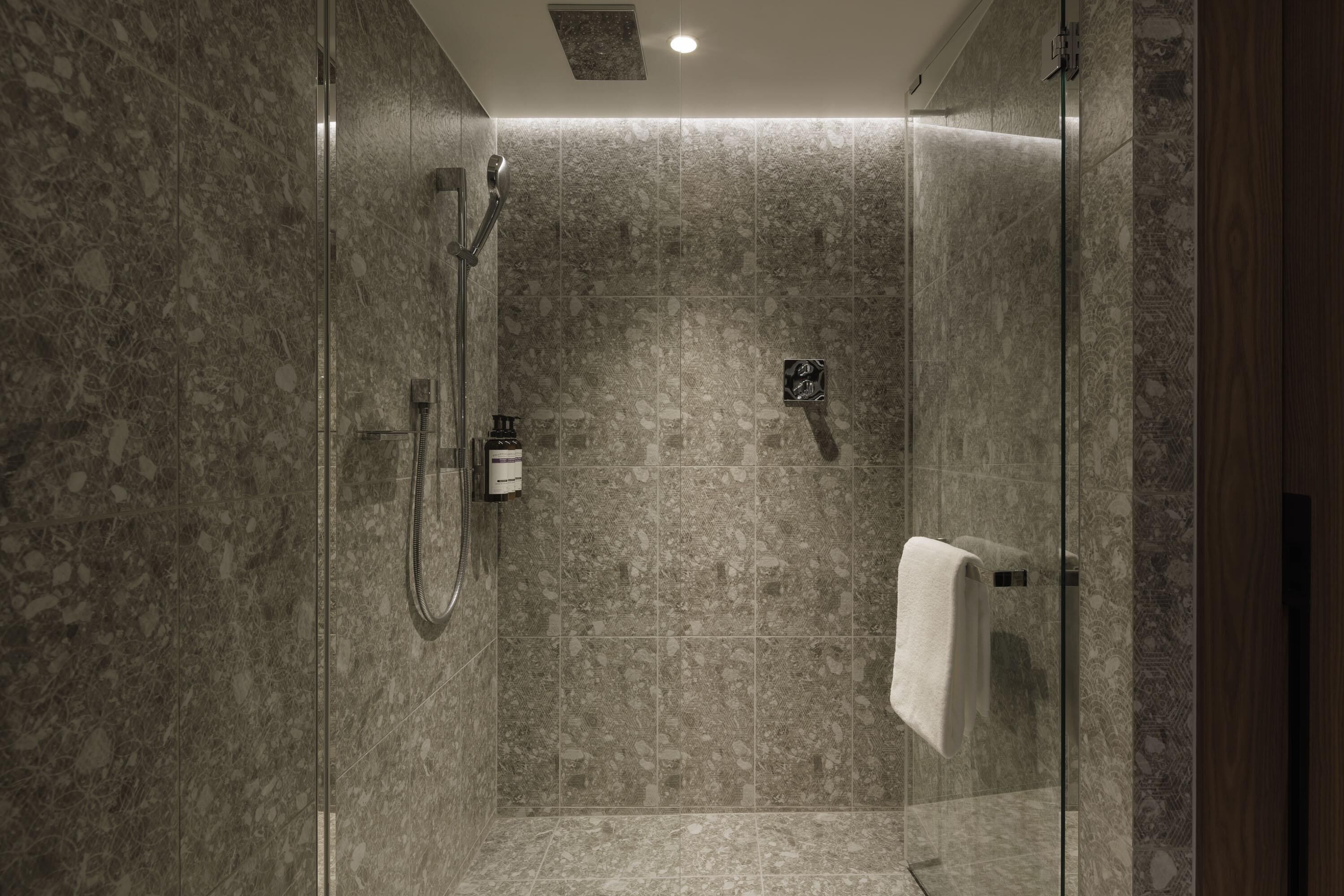 Eine moderne Dusche mit Glastür, Handbrause und Handtuchhalter.