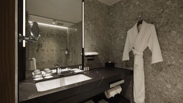 Un baño moderno con un espejo grande, encimera de mármol oscuro y una bata colgada en la pared.