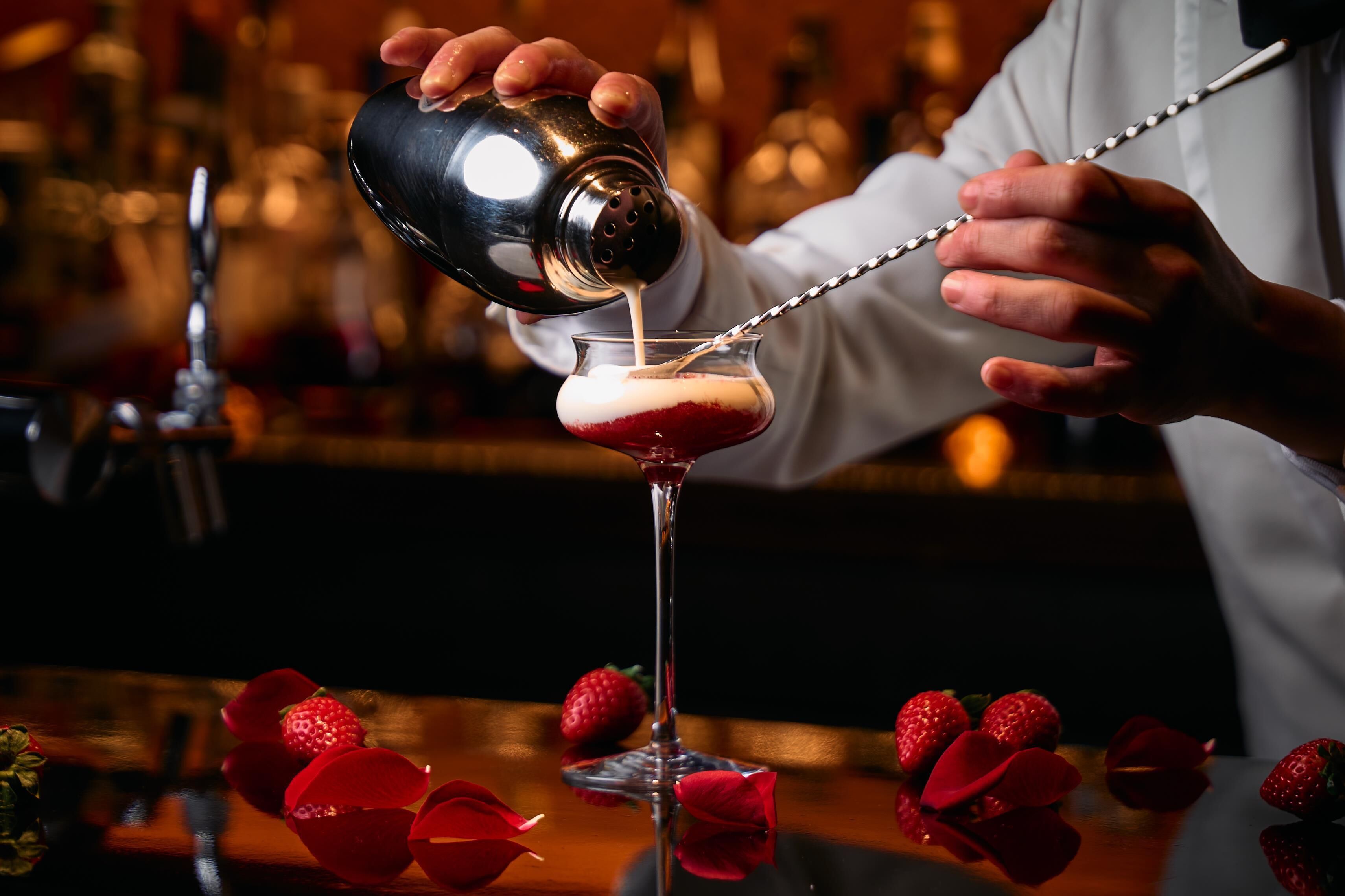 A bartender pouring a drink into a glass with a straw.