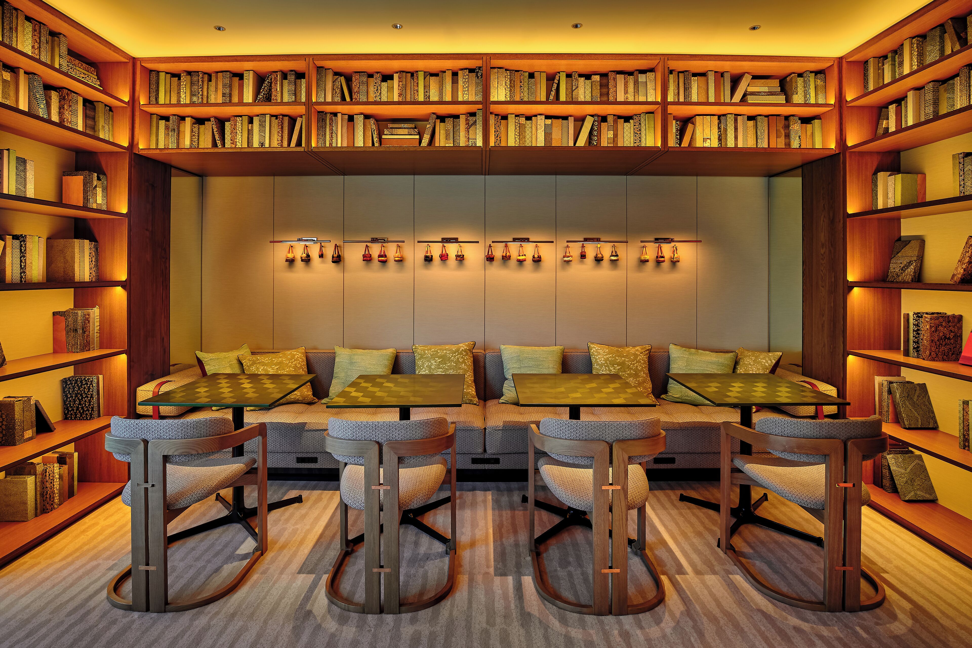 A library with bookshelves, a seating area with tables and chairs, and a wall-mounted light fixture.