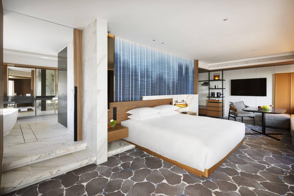A modern hotel room with a large bed, a TV, a desk, and a bathroom with a bathtub.