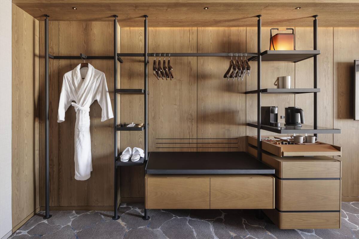 A compact hotel room with a wooden wardrobe, a black desk, and a hanging robe.