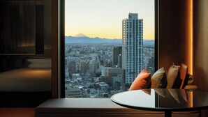 A room with a large window offering a cityscape view, a round table with cushions, and a wooden cabinet.
