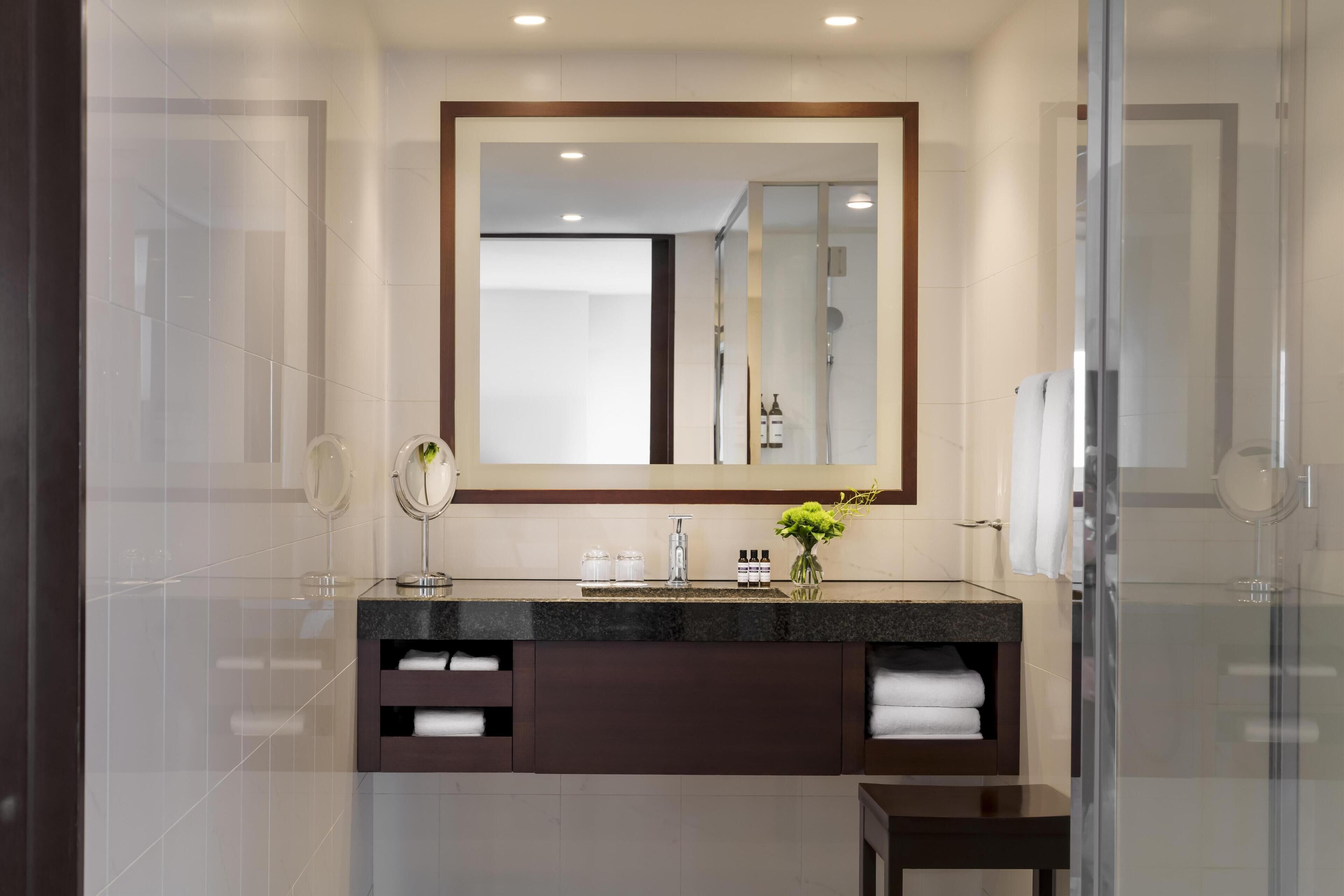 Un baño moderno con un espejo grande, un tocador con encimera oscura y una cabina de ducha con paredes de vidrio.