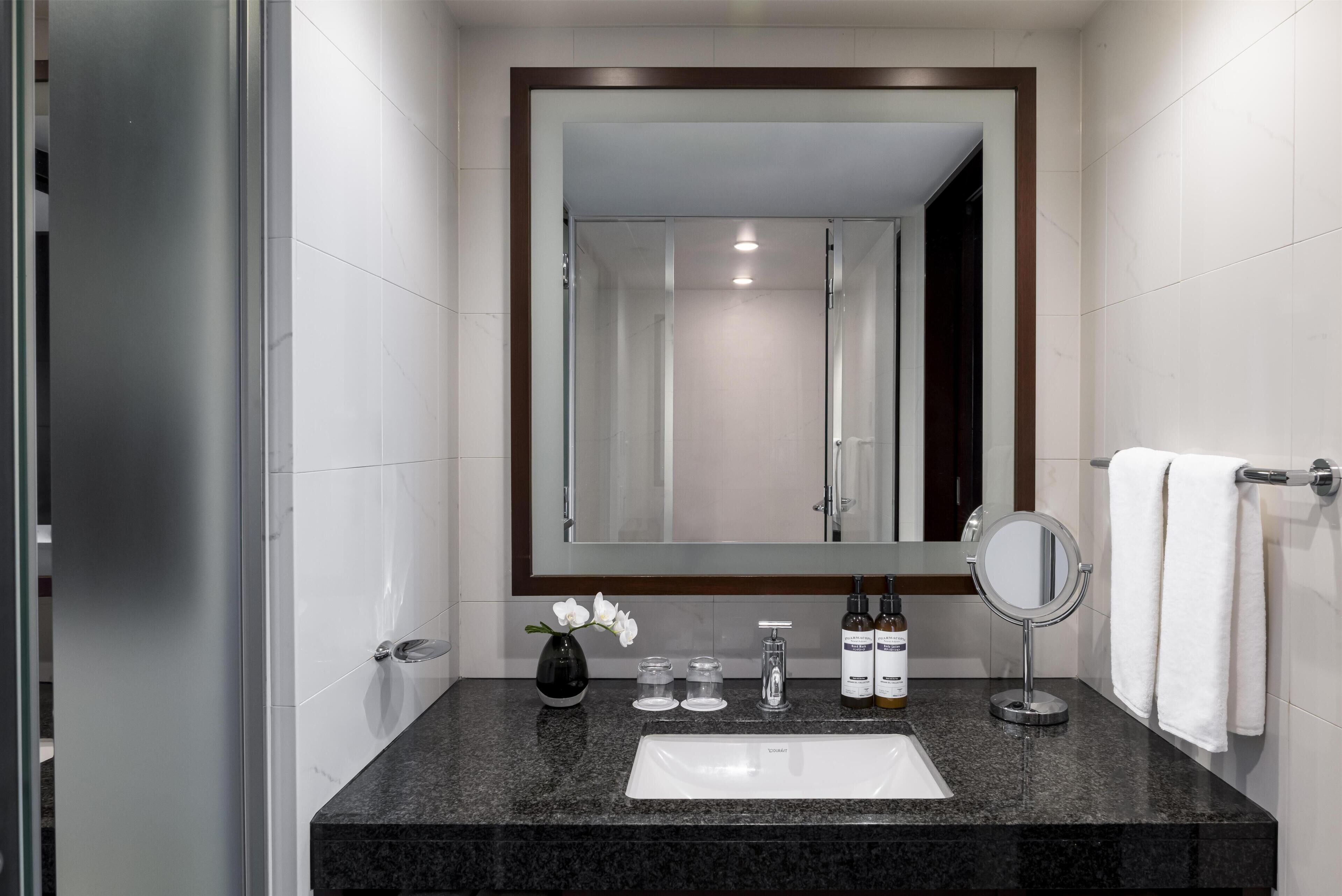 A modern bathroom with a granite countertop, a white sink, a large mirror, and a towel rack.