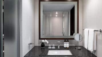 A modern bathroom with a granite countertop, a white sink, a large mirror, and a towel rack.