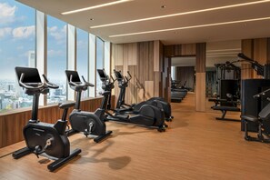 A modern gym with cardio machines, weightlifting equipment, and large windows offering city views.