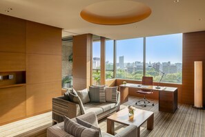 A modern living room with a sofa, coffee table, and desk, large windows with a city view, and a wooden accent wall.