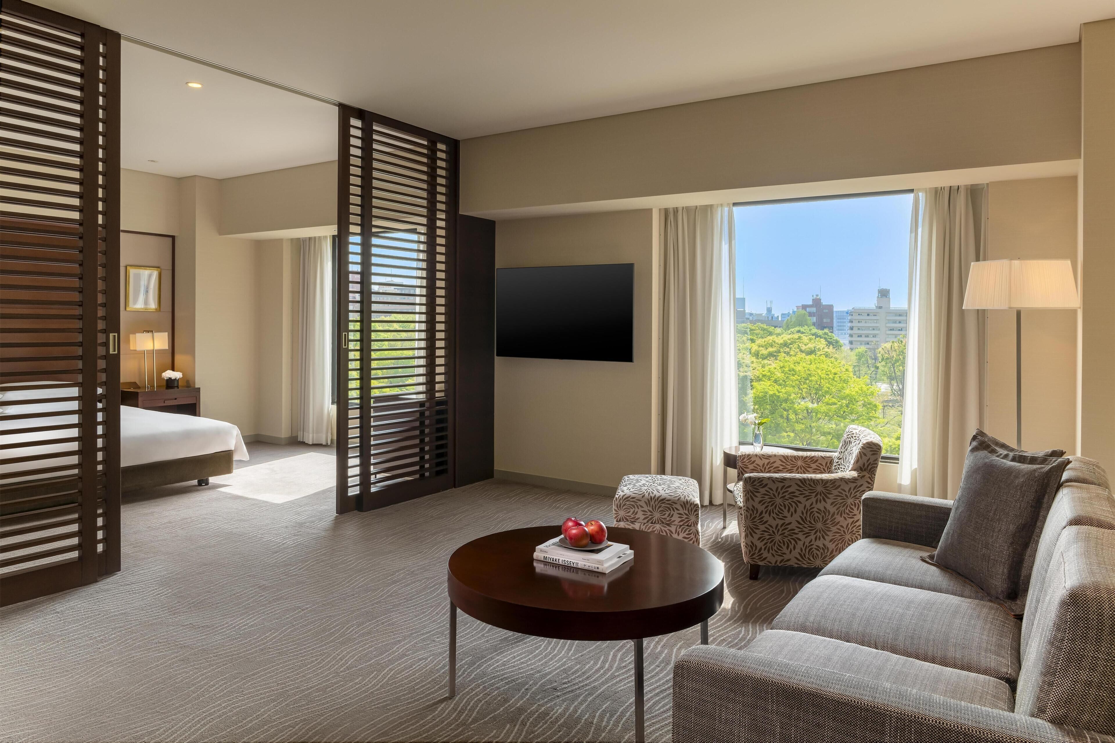 A hotel room with a bed, a sofa, a coffee table, a TV, and a window with a city view.