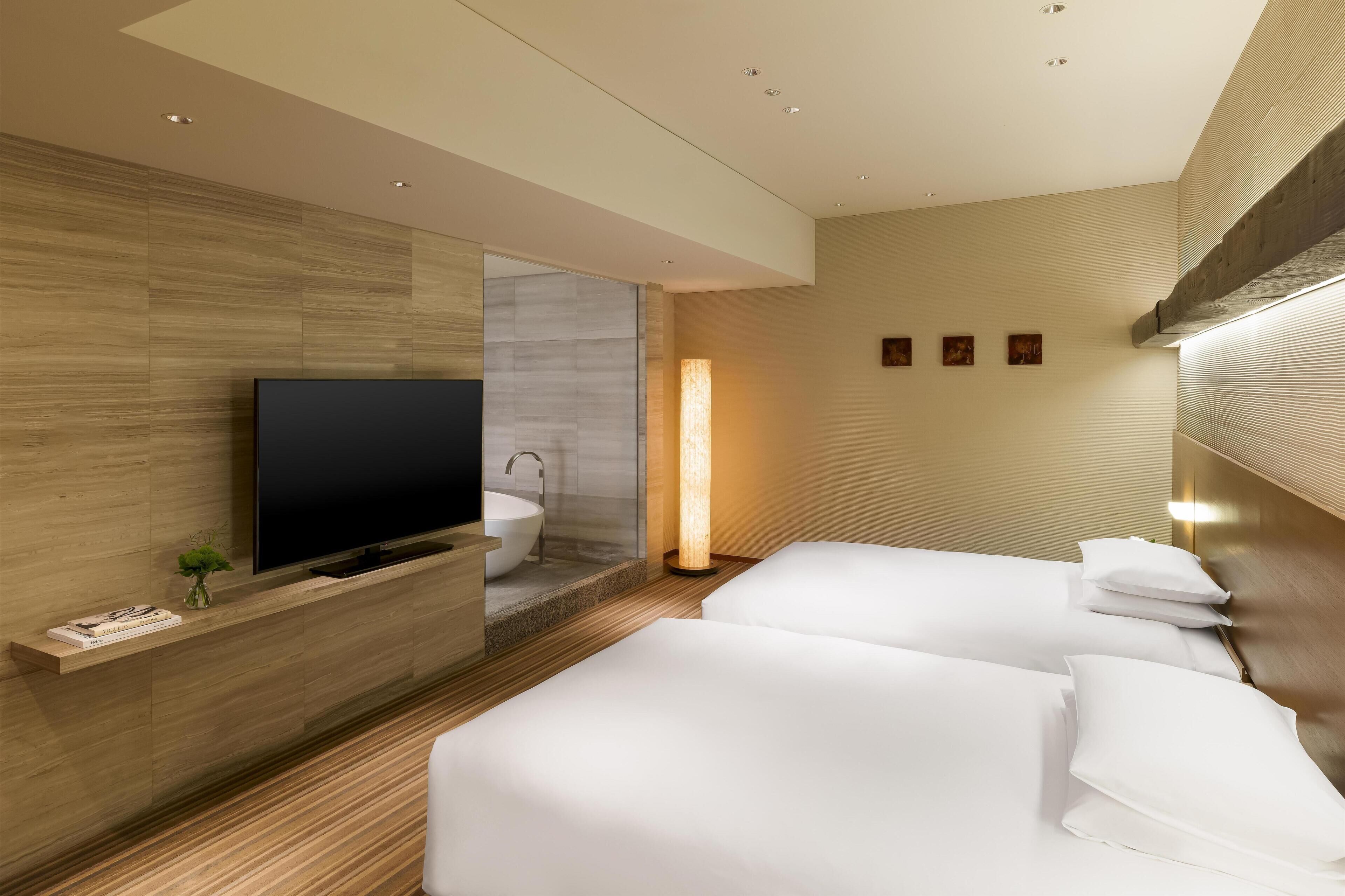 A hotel room with a flat-screen TV, a large window, a sink, and two beds.