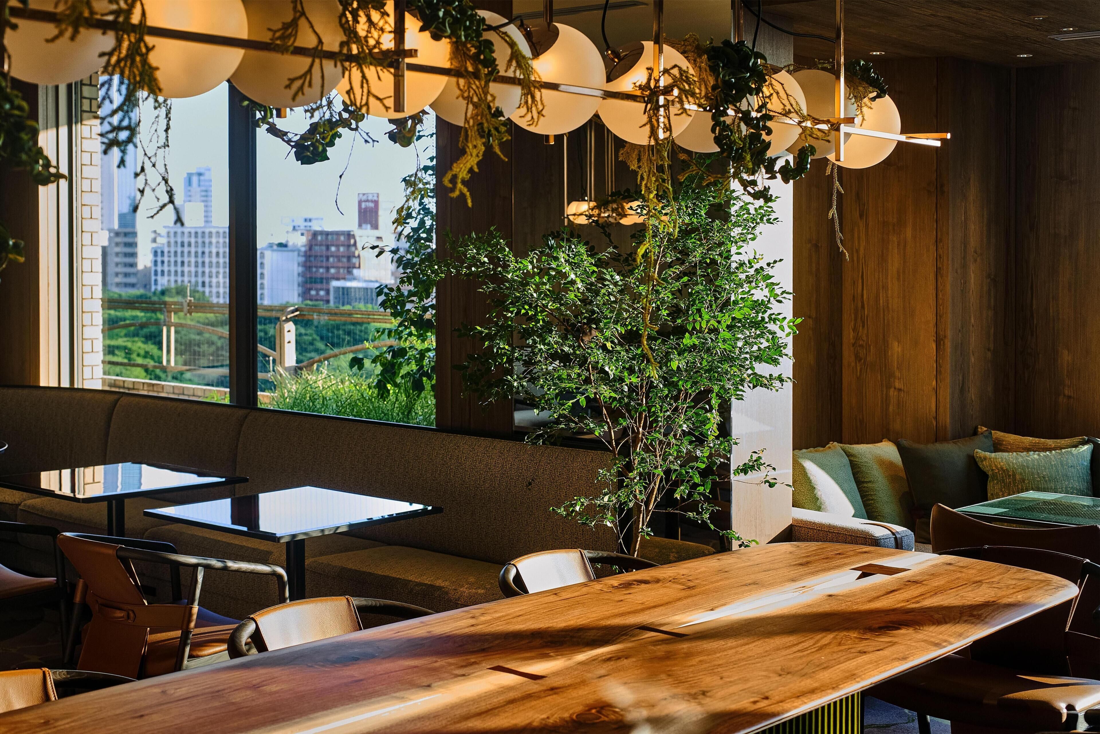 A modern interior with a wooden dining table, seating arrangements, and a view of a cityscape through large windows.