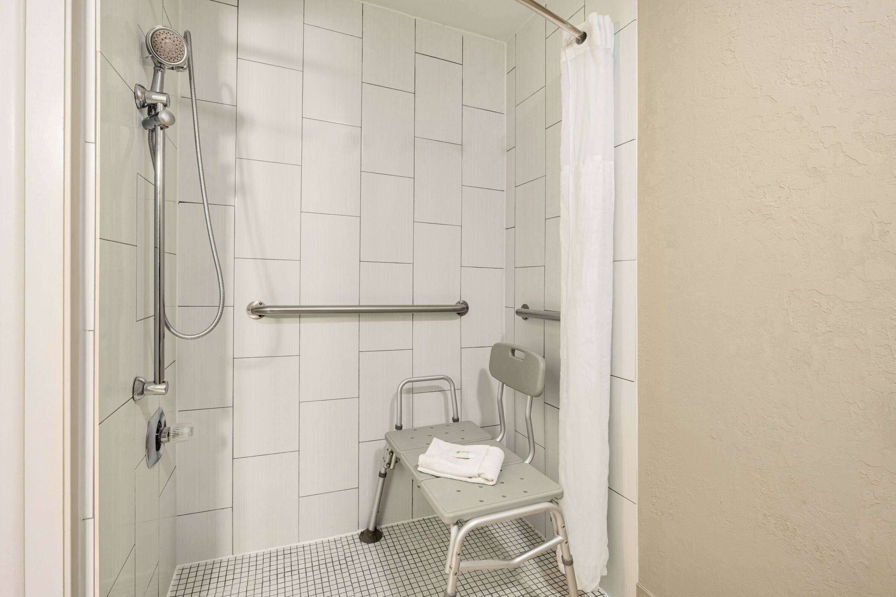 A shower area with a grab bar, a wheelchair, and a showerhead.