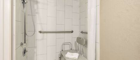 A shower area with a grab bar, a wheelchair, and a showerhead.