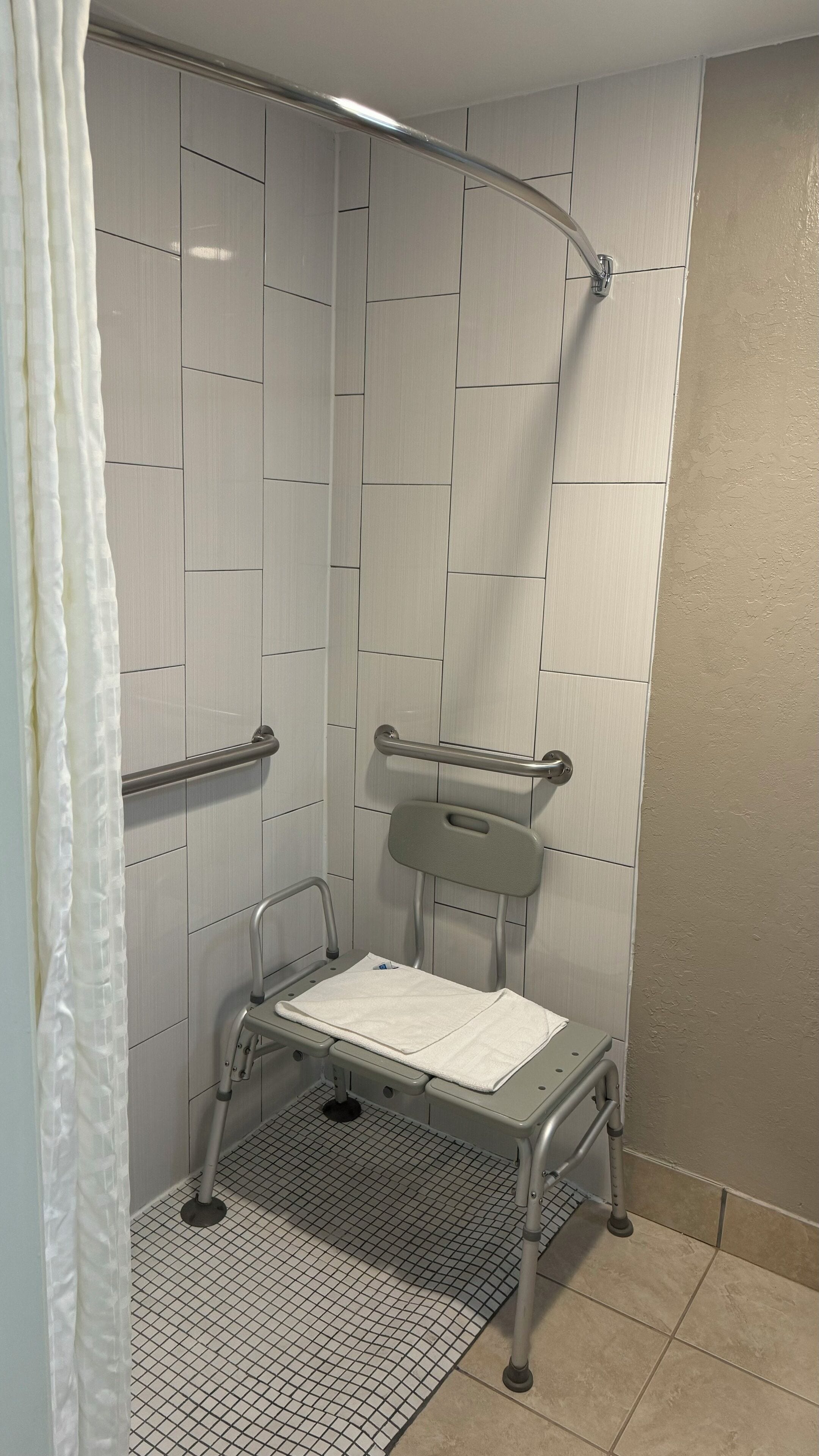 A shower area with a grab bar, a shower seat, and a shower curtain.