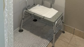 A shower area with a grab bar, a shower seat, and a shower curtain.