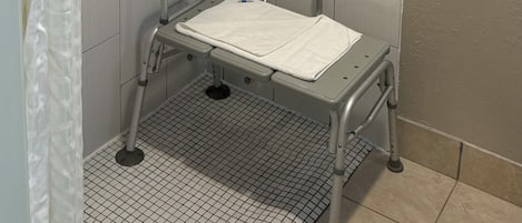 Zona de ducha con barra de apoyo, asiento y cortina.