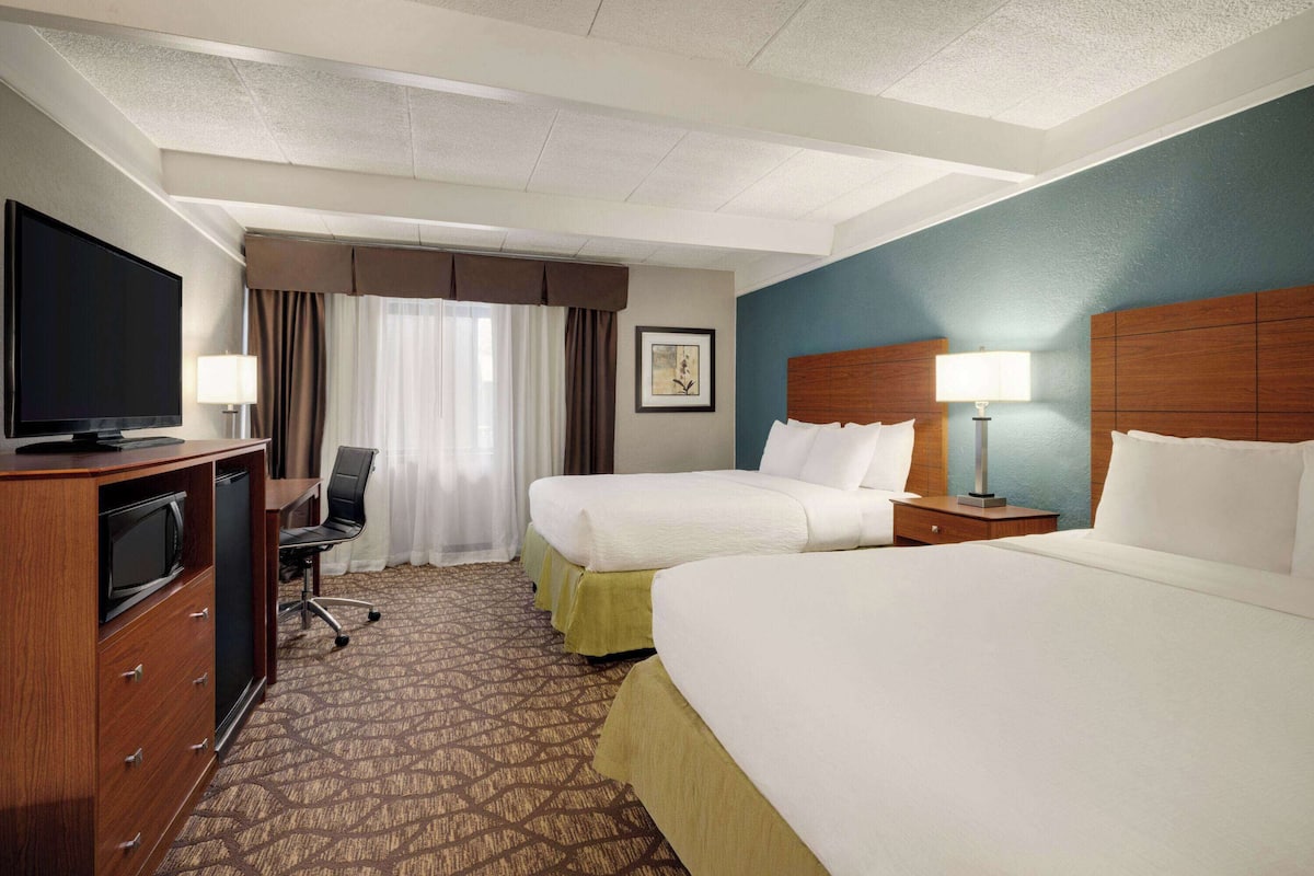 A hotel room with two beds, a desk with a television, and a chair.