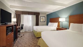 A hotel room with two beds, a desk with a television, and a chair.