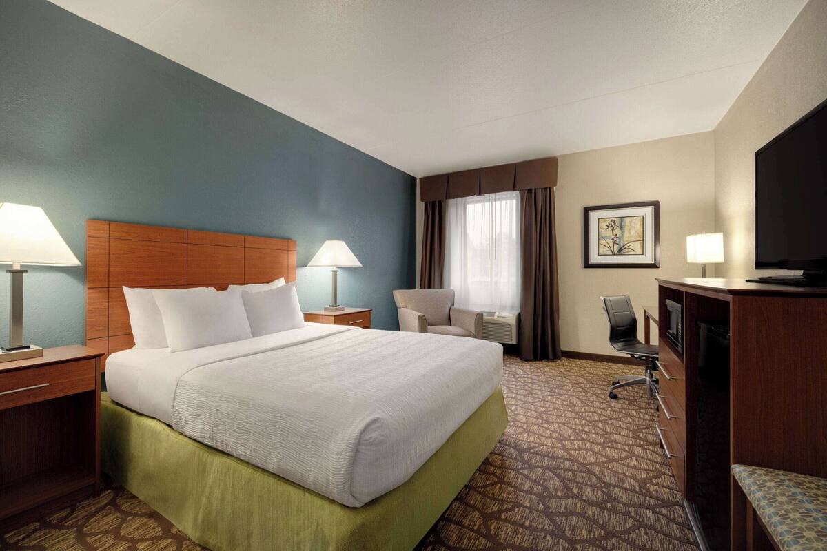 A hotel room with a large bed, two bedside tables with lamps, a desk with a chair, a television, and a framed picture on the wall.