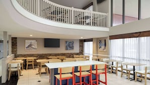 A spacious dining area with multiple tables and chairs, a central island with seating, and a staircase leading to an upper level.