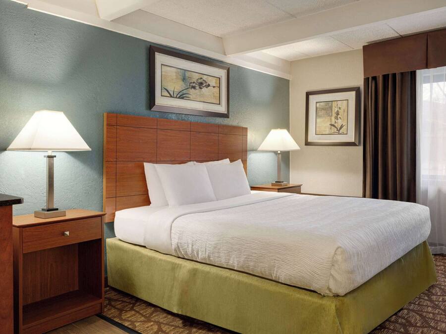 Una habitación de hotel con una cama grande, dos mesitas de noche con lámparas, un cabecero de madera y obras de arte en las paredes.