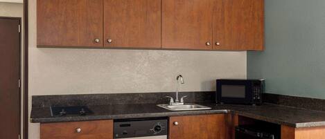 Una cocina compacta con armarios de madera, lavavajillas, microondas y un lavabo.