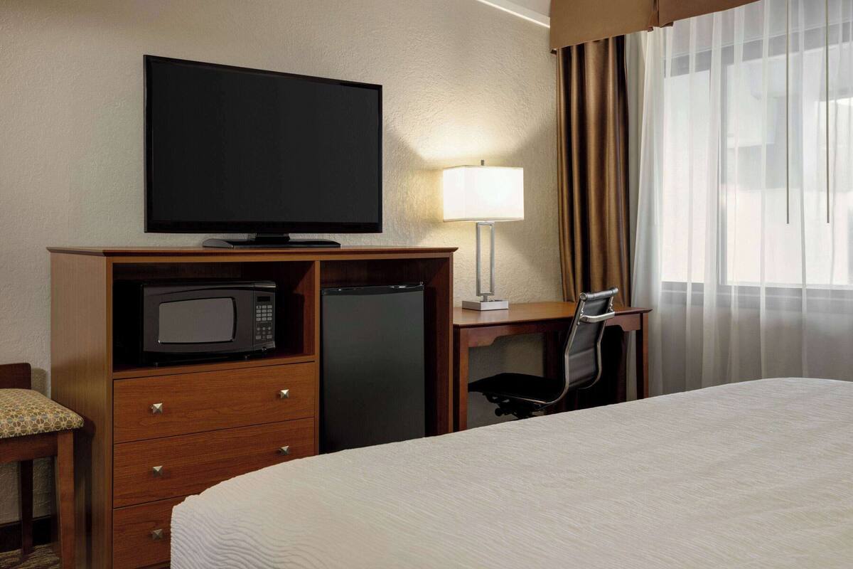 A hotel room with a bed, a desk with a computer, a TV, a microwave, and a refrigerator.