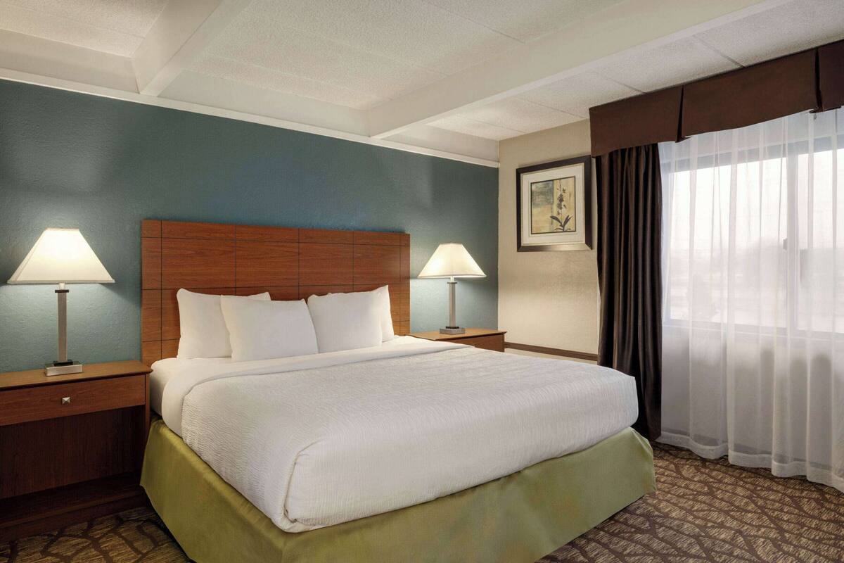 A hotel room with a large bed, two bedside tables with lamps, a framed picture on the wall, and a window with curtains.