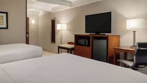 A hotel room with two beds, a television, a desk with a chair, and a lamp.