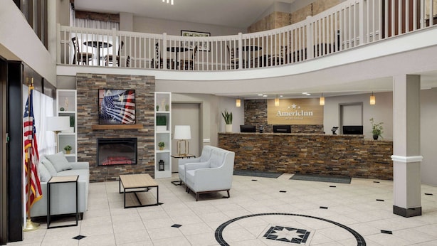 A hotel lobby with a reception desk, a fireplace, seating area, and a balcony.