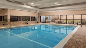 An indoor swimming pool with clear lanes, a brick floor, and a seating area with tables and chairs.