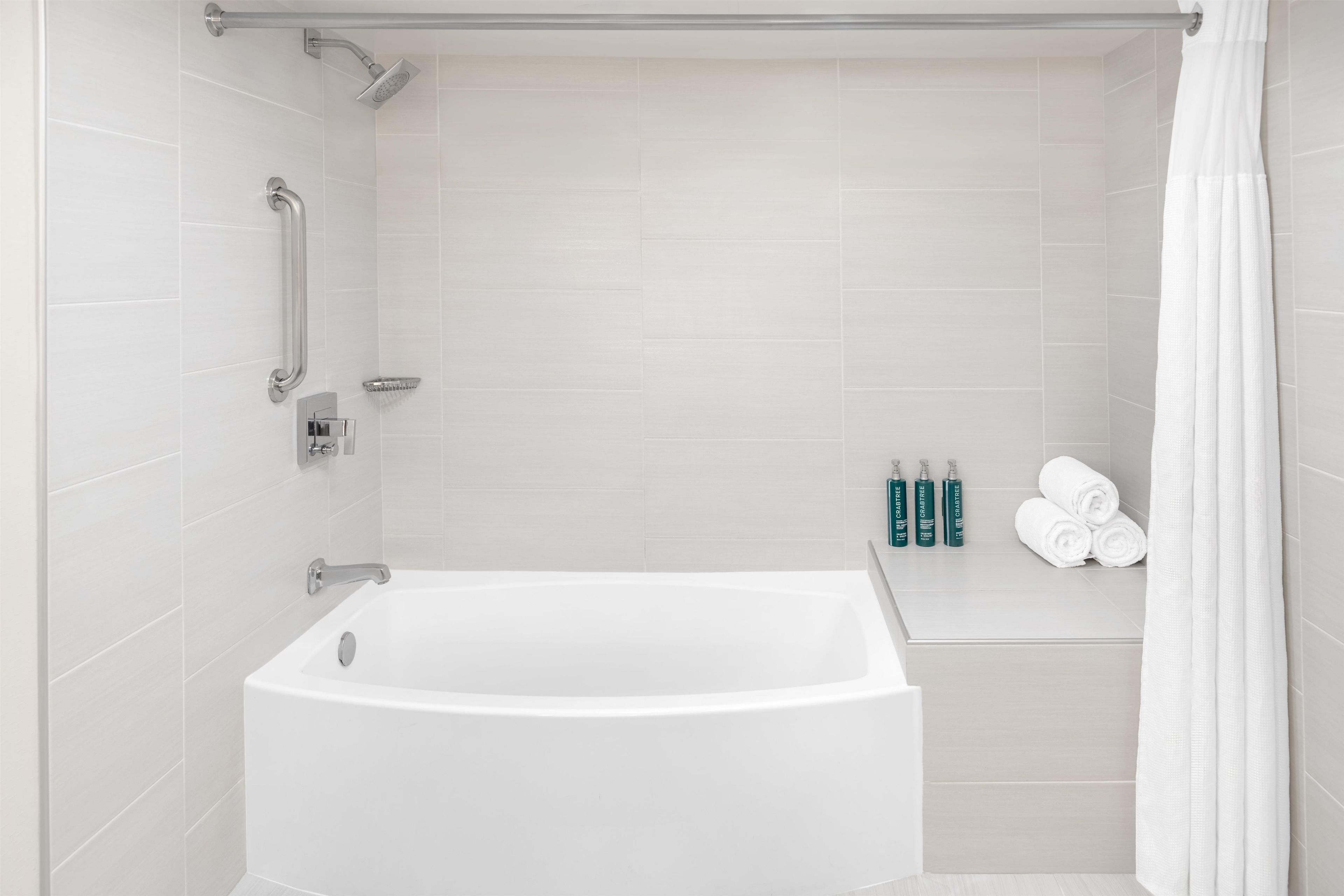 A modern bathroom with a freestanding bathtub, grab bars, a handheld showerhead, and a towel rack with folded towels.