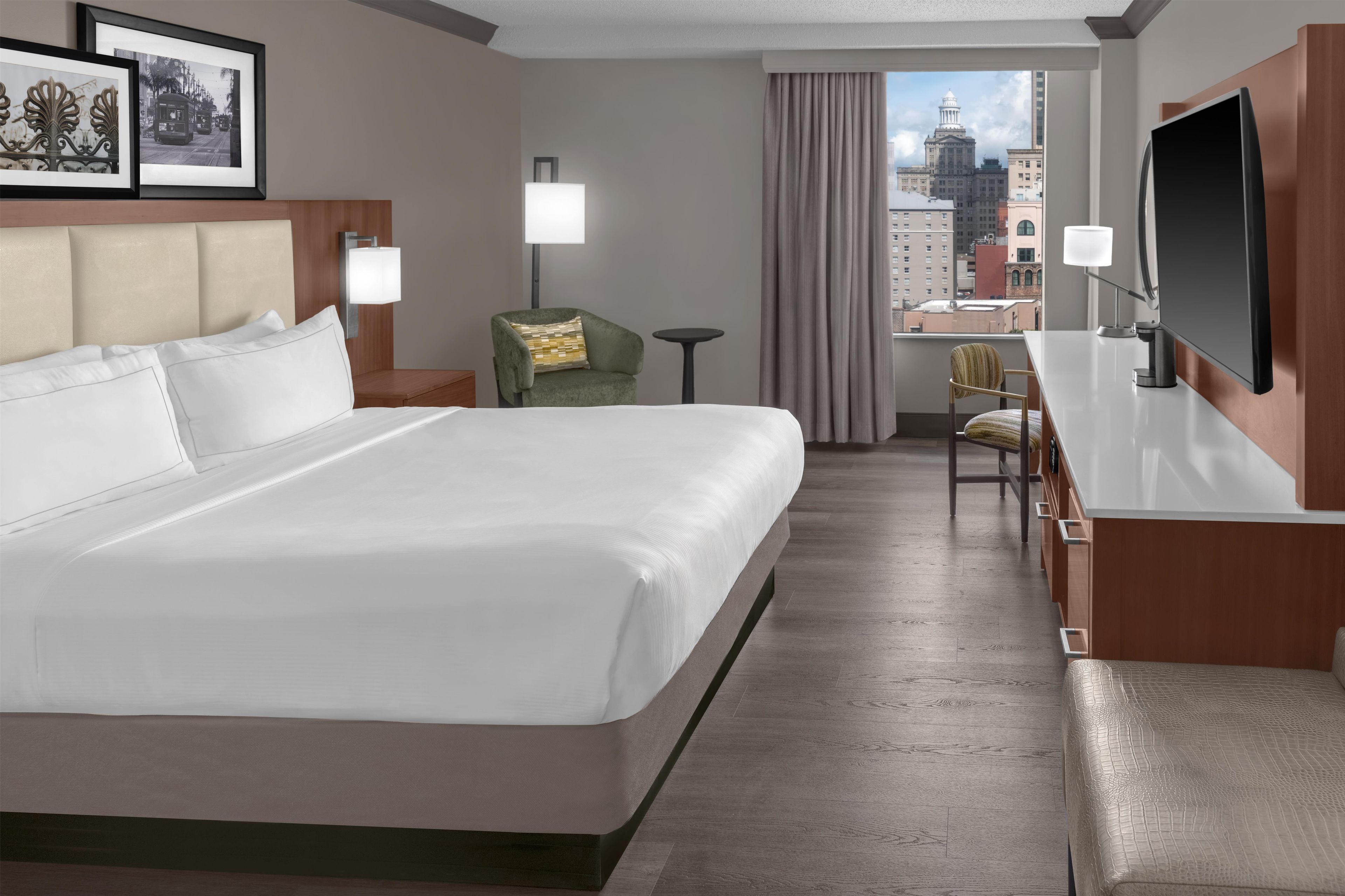 Habitación de hotel con una cama grande, un escritorio, una silla, un televisor y vistas a la ciudad.